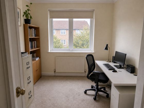 Small British home office with a basic flat-pack desk, visible cables, mismatched storage, radiator and uPVC window before redesign.