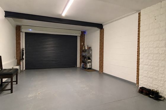 British semi-detached garage with a black up-and-over door, exposed brick pillars and a steel beam before conversion.