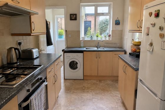 Original compact British galley kitchen with a freestanding white fridge, exposed washing machine and cluttered worktops before its remodel.