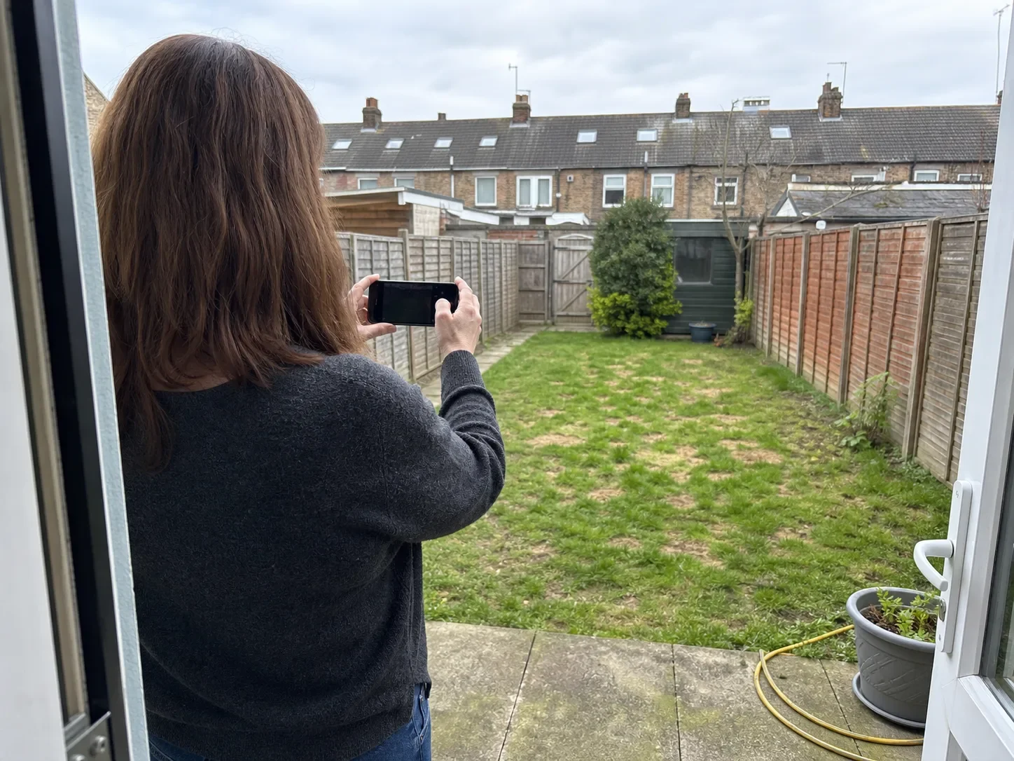 A homeowner photographing a modest back garden from the house